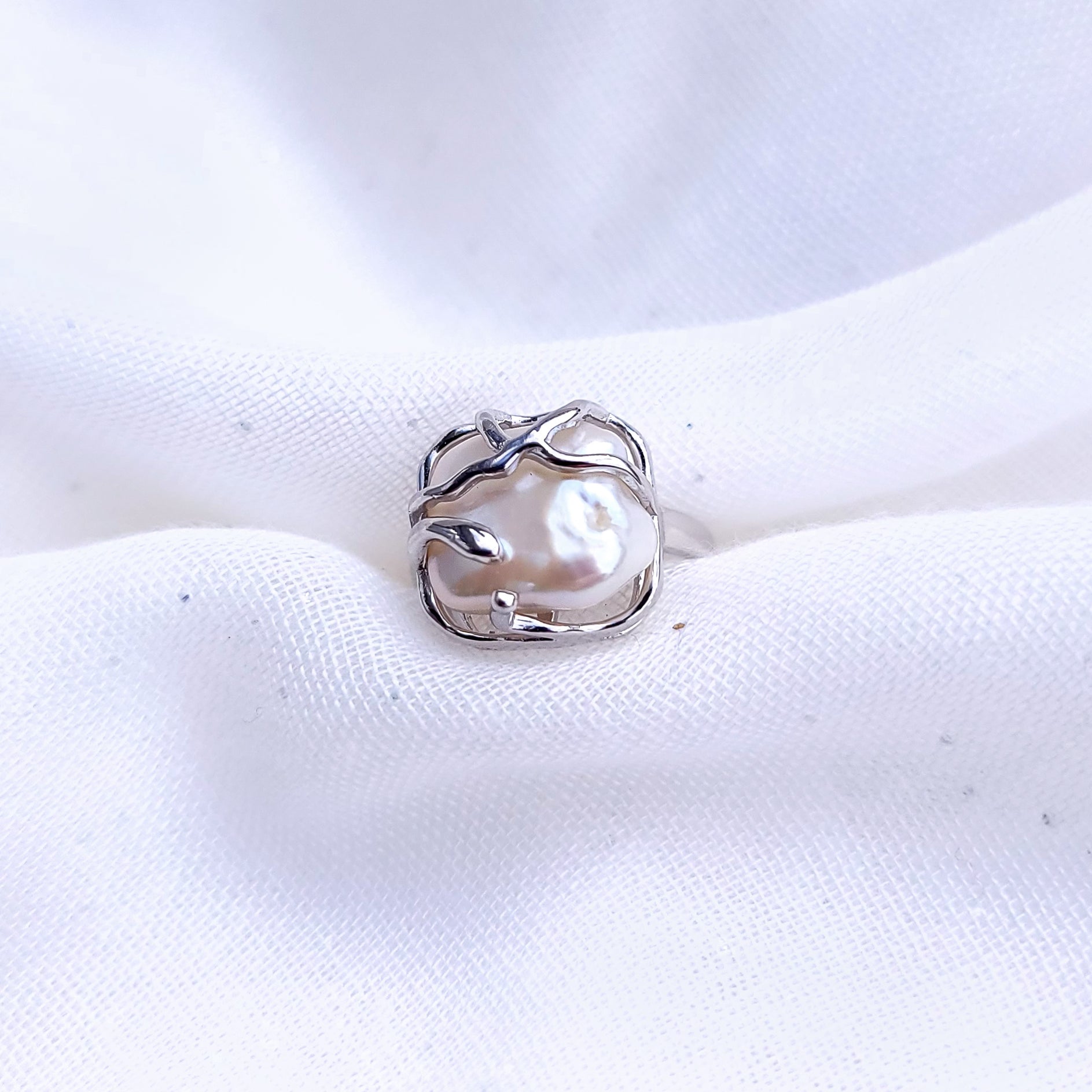 Crafted from sterling silver, the Baroque Elegance adjustable ring offers a versatile style that can be worn independently for a minimalist look or layered with other rings to create a fashionable statement. This ring beautifully is crafted from Sterling Silver and presents a square baroque-style lab pearl, painstakingly handcrafted to achieve perfection, guaranteeing a flawless finish and an exquisite presentation.