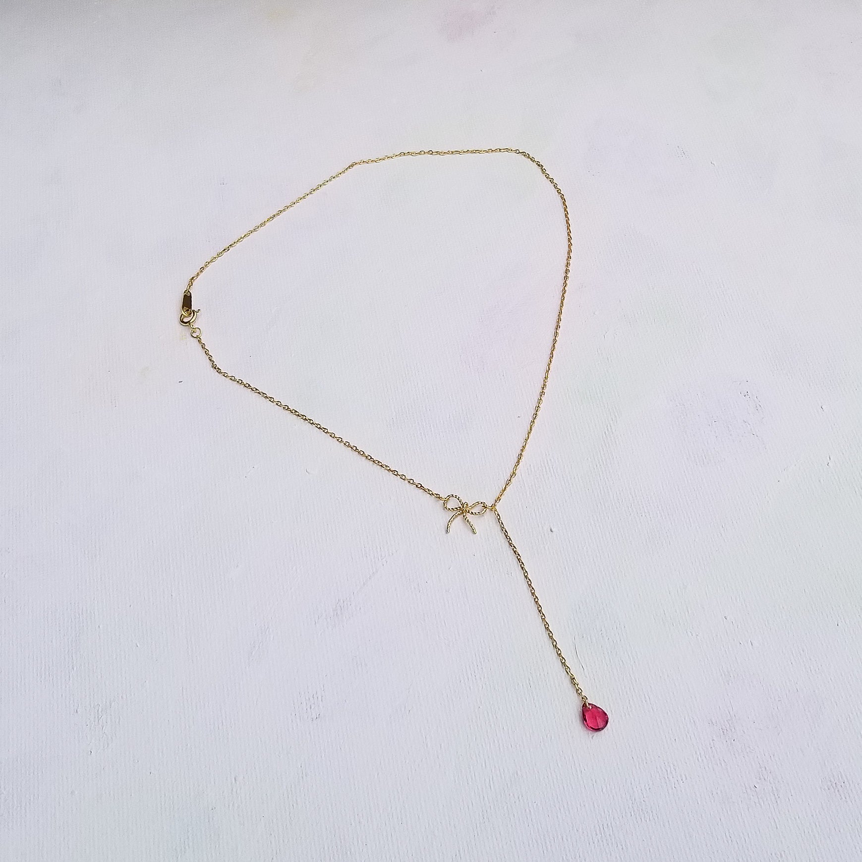 This beautiful choker - lariat style necklace features an elegant bow and a tear cut red zirconia stone. The details really stand out on this necklace. The slender chain and delicate profile make it the ideal everyday piece and it can also be a centerpiece for a special occasion. Material: 14K Gold Plated over 925 Sterling Silver Stone: Red Cubic Zirconia Style: Choker Style Necklace - Bowknot, Tassel Chain Length: 16 Inch Nickel & Lead free & Hypoallergenic